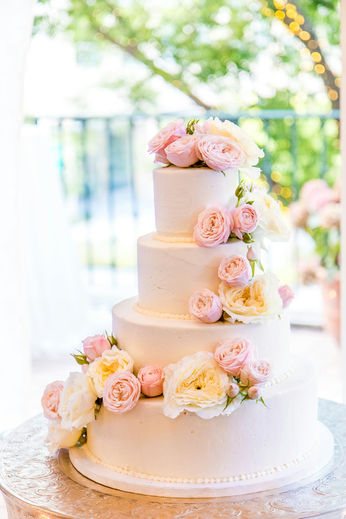 A four-tier white wedding cake dressed with blush and peach garden roses